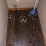 Bathroom floor with toilet removed, exposing drain flange and plumbing tools