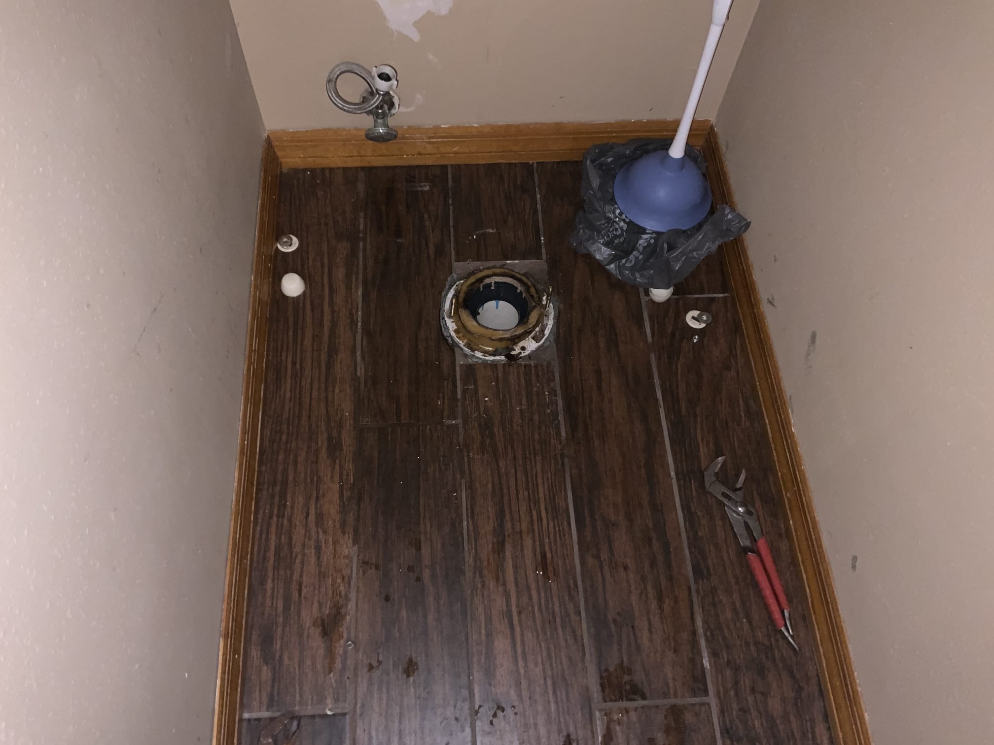 Bathroom floor with toilet removed, exposing drain flange and plumbing tools